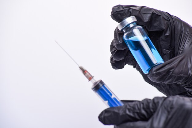 the doctor's hand holds an ampoule with blue liquid and a syringe.  syringe out of focus. Vaccination concept