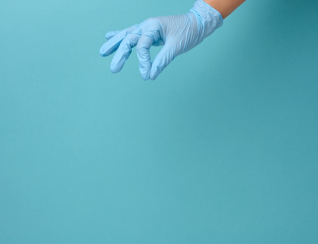 Doctor's hand in een blauwe medische handschoen houdt een object op een blauwe achtergrond. Kopieer de ruimte, houd een willekeurig object vast