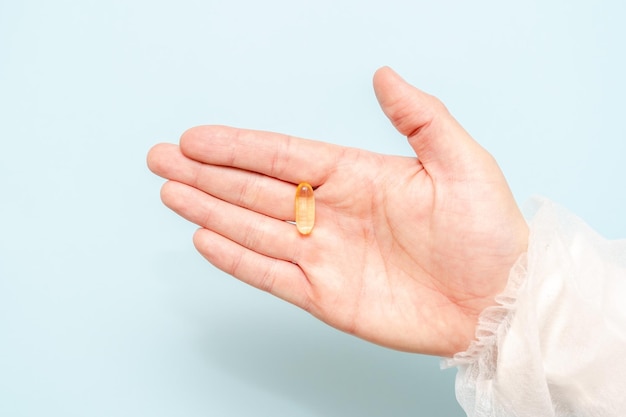 Doctor's hand met een visoliecapsule Omega 3 of pil geïsoleerd op lichtblauwe achtergrond