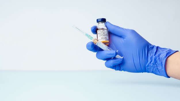 A doctor's hand wears a medical glove holding a syringe and a dose vial of the covid 19 corona virus vaccine for injection.