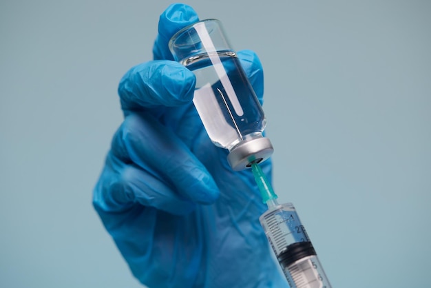 The doctor's hand wears a medical glove holding a syringe while taking a liquid vaccine from a vial about to be injected Injection vaccination concept