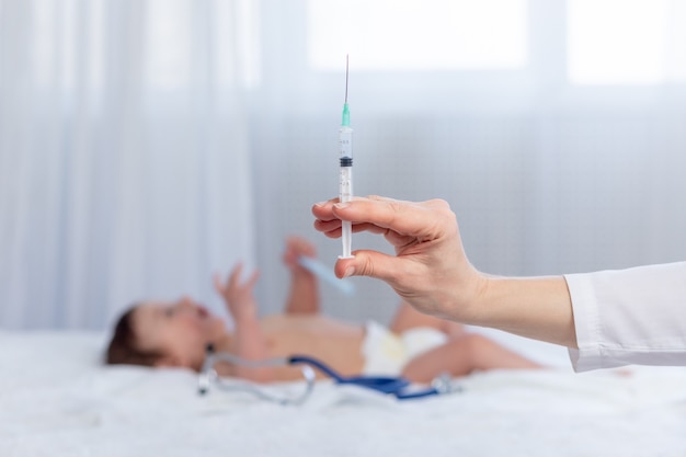 A doctor's hand with a syringe on the background of a small child, a pediatrician gives an injection to an infant