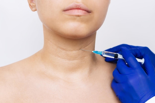 Doctor's hands in blue gloves hold syringe needle for lifting procedure on woman's neck with wrinkle