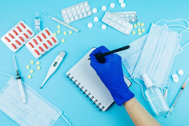 Doctor's hands in blue gloves. medicine for coronavirus. Medicines in the fight against Covid-19. Pills, syringes, thermometer, medical mask on blue table. 