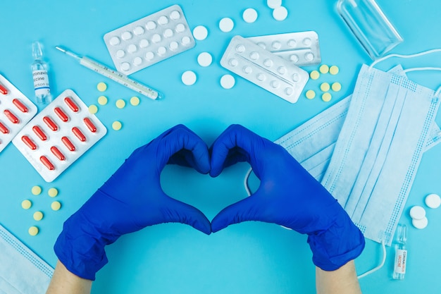 Doctor's hands in blue gloves. medicine for coronavirus.
medicines in the fight against covid-19. pills, syringes,
thermometer, medical mask on blue table.