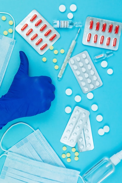 Doctor's hands in blue gloves. medicine for coronavirus. Medicines in the fight against Covid-19. Pills, syringes, thermometer, medical mask on blue table. 