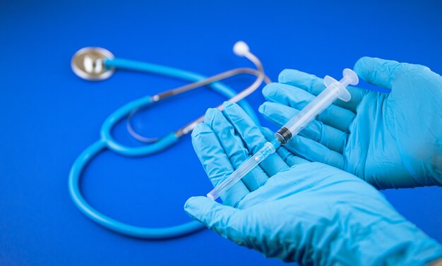 Doctor's hands in blue medical gloves holding a plastic syringe on blue background