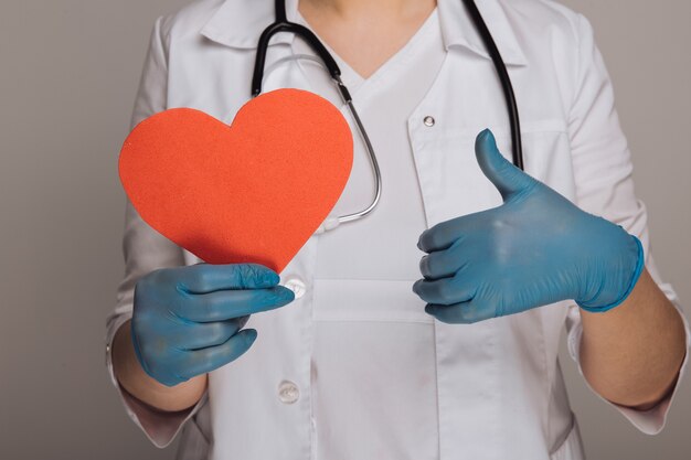 Doctor's hands in gloves holding image of heart. stethoscope around the neck