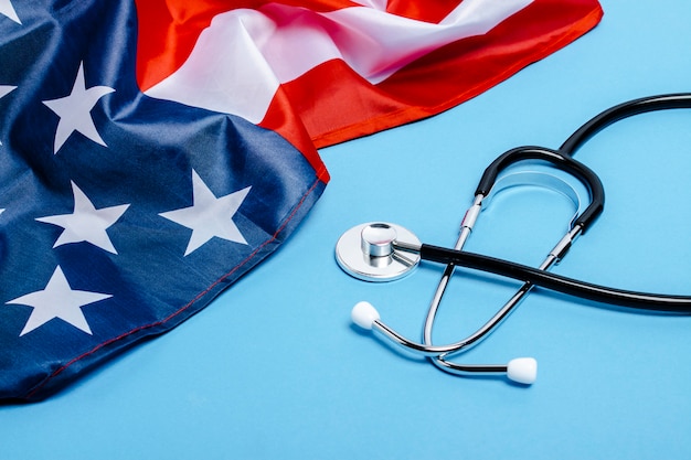 Doctor's stethoscope and US flag on a blue surface. USA medicine concept, high level, medical insurance, best medicine, vaccine, virus, epidemic. Flat lay, top view