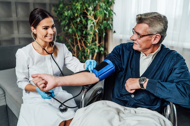 A doctor's visit home, the doctor measures the blood pressure of a patient sitting in a wheelchair.