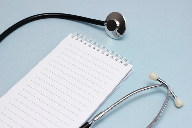 Il posto di lavoro del medico. uno stetoscopio e un quaderno per scrivere con una pagina pulita. medicina e concetto di salute.