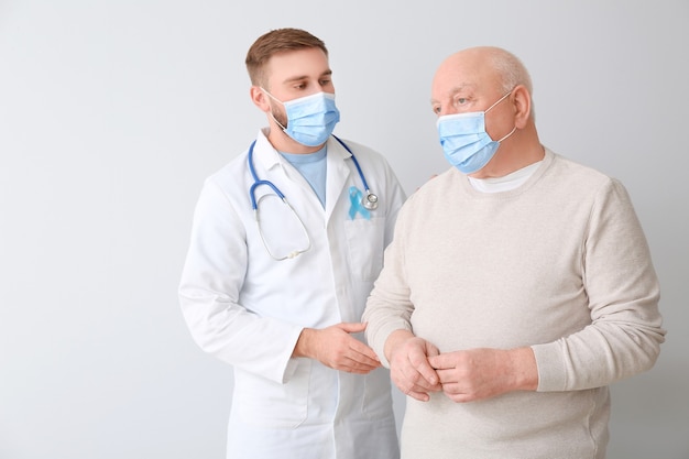 Doctor and senior man on light background. Prostate cancer awareness concept