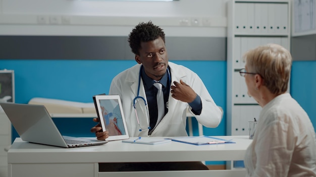 Doctor and senior patient looking at heart picture on modern tablet screen for examination and understanding cardiology. sick old woman and medic analyzing virtual cardiogram at desk