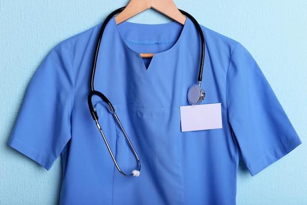 Foto camicia medico con stetoscopio su appendiabiti su sfondo blu