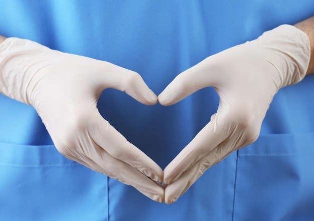 Doctor showing shape of heart by his hands in sterile gloves closeup view