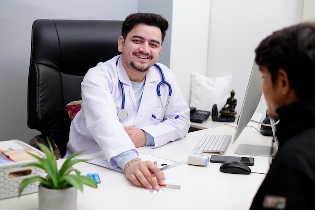 A doctor sits at a desk with a man in a white coat and a laptop.