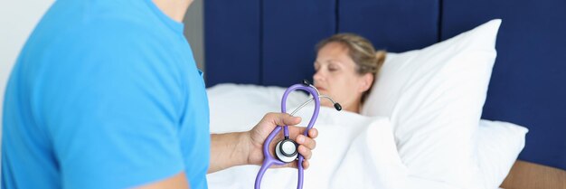 Doctor sitting on patient bed and holding stethoscope in his hands hospital treatment concept