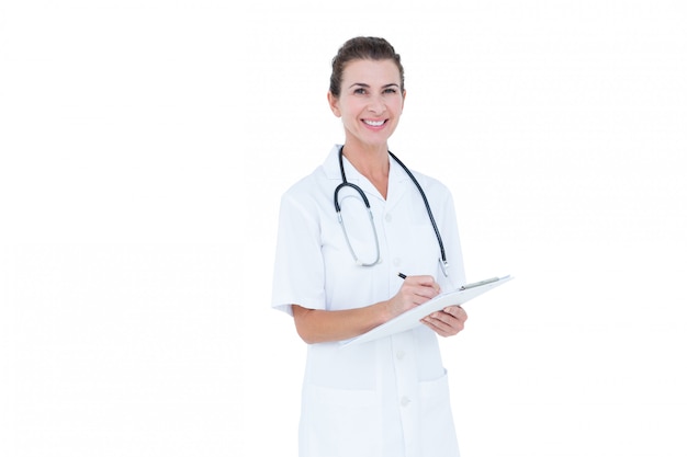  Doctor smiling and holding clipboard and pen against a white wall 