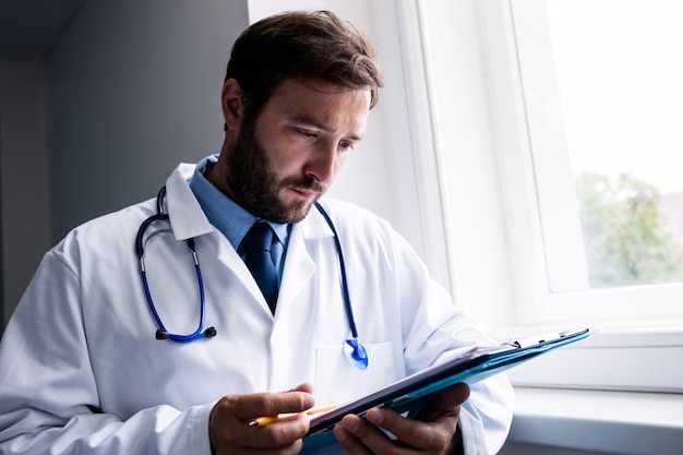 Doctor standing in corridor looking at clipboard