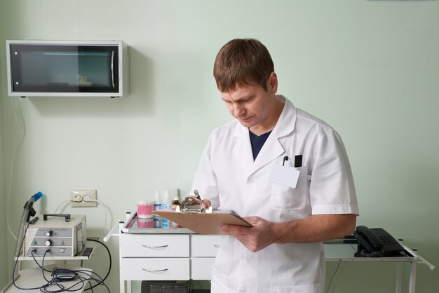 Doctor standing in his laboratory, holding clipboard and writing diagnosis