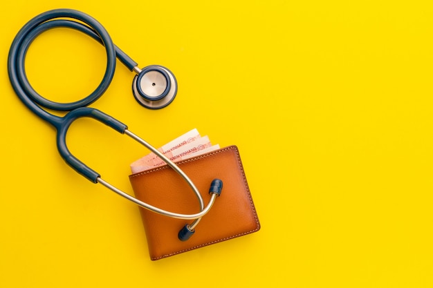 Doctor stethoscope and the new leather brown men wallet on yellow. budget for health check or money and financial concept