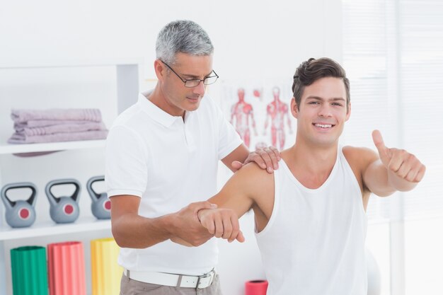 Doctor stretching a young man arm with thumb up 