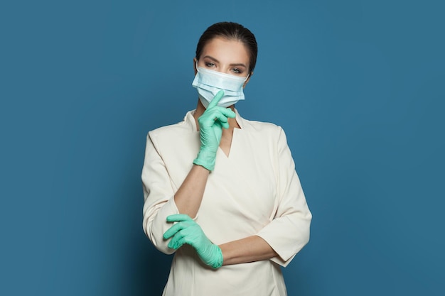 Doctor surgeon in protective medical mask and surgical gloves on blue background