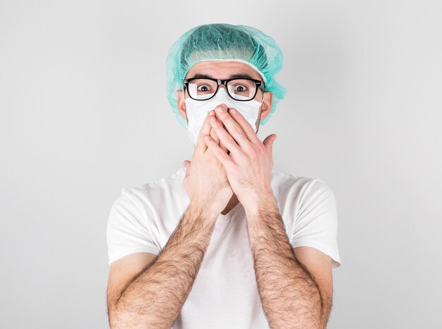 Doctor surgeon in white medical mask and a medical cap stands over white background with surprise