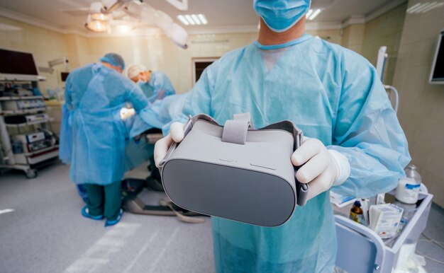 Doctor in a surgical room with virtual reality glasses on the background of the real operation.