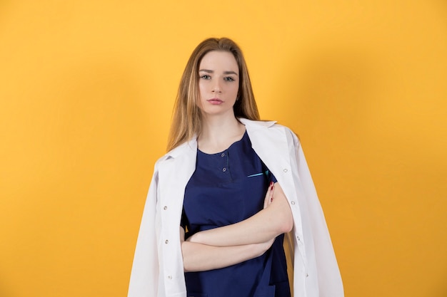 Doctor in a surgical suit and white coat on a yellow background