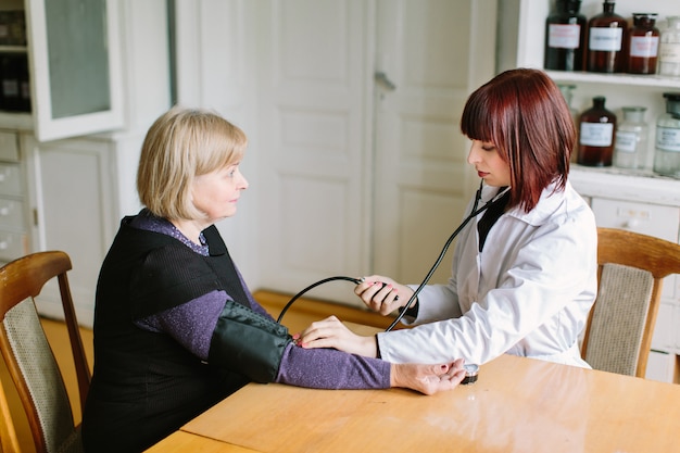 Doctor taking blood pressure of female patient at office