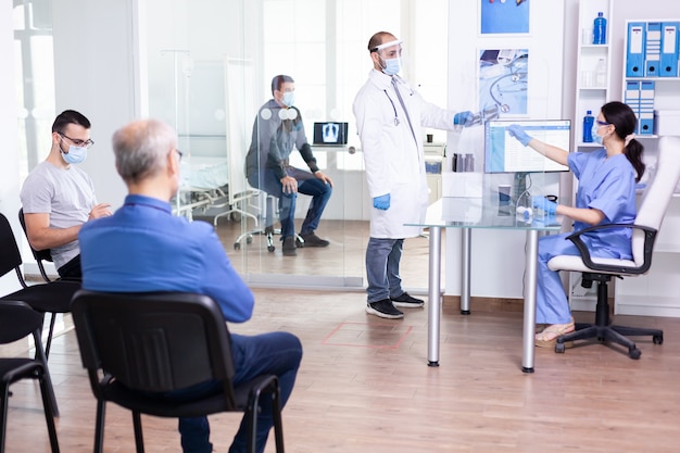 Doctor taking patient x-ray from nurse wearing face mask and visor against cornavirus global pandemic and group of people are waiting for examination