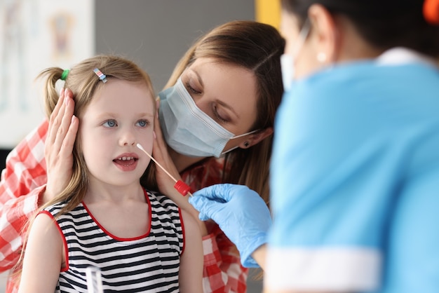 Doctor taking pcr swab from nose of little girl using cotton swab at clinic