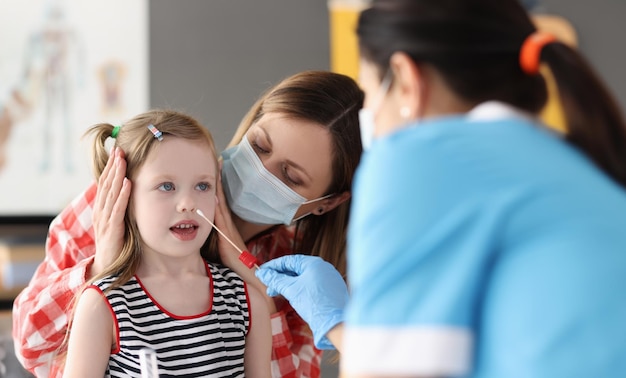 Doctor taking pcr swab from nose of little girl using cotton swab at clinic