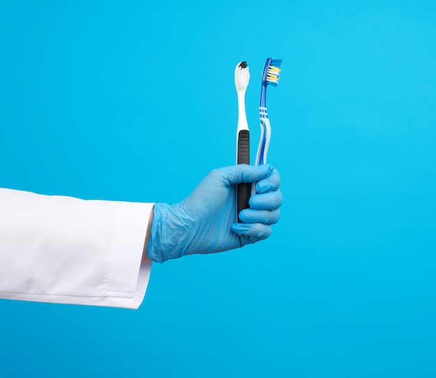Врач-терапевт одет в белую форму халата и синие стерильные перчатки с зубной щеткой