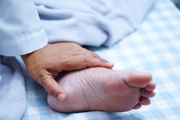 Doctor touching foot of Asian senior woman patient with love, care, encourage and empathy.