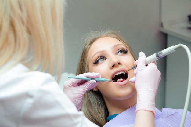 Doctor in uniform checking up female patient's teeth in dental c