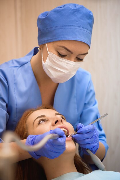 Medico in uniforme che controlla i denti del paziente femminile in clinica dentale
