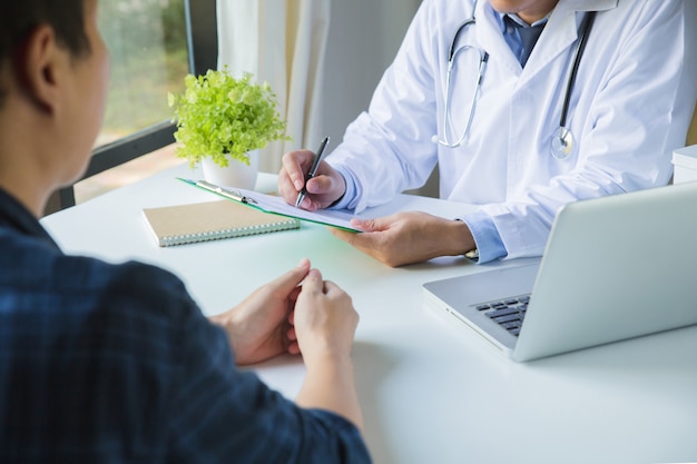 Doctor using a clipboard to fill out a medical history of a young man's medication and patient discussing the results of a physical examination in a clinic