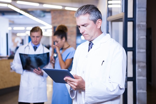 Doctor using digital tablet in hospital and colleagues standing behind and discussing