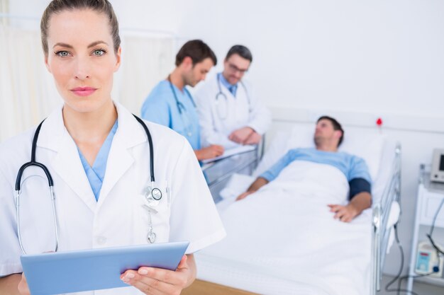 Doctor using digital tablet with colleagues and patient behind