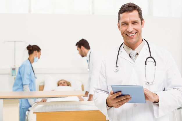 Doctor using digital tablet with colleagues and patient behind