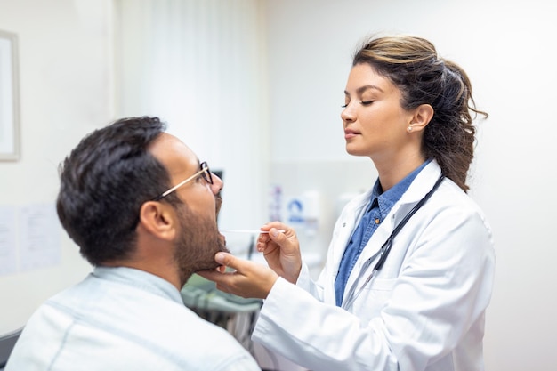 Foto medico che utilizza la spatola di ispezione per esaminare la gola del paziente medico orl che esegue l'esame della gola di un paziente uomo ha aperto la bocca al controllo della gola