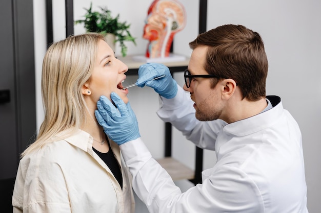 Doctor using inspection spatula to examine patient throat ENT doctor doing throat exam of a woman Patient opened her mouth to throat checkup