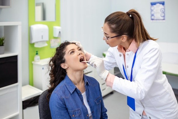 Doctor using inspection spatula to examine patient throat ENT doctor doing throat exam of a woman patient opened her mouth to throat checkup