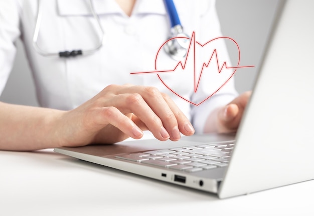Врач использует ноутбук и смотрит на тест электрокардиограммы, проверяя признаки сердечных заболеваний Кардиолог отправляет результаты ЭКГ и рекомендации пациенту через Интернет
