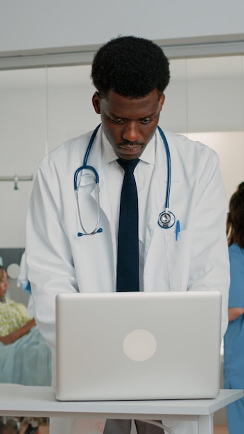 간호사가 검진 파일을 돕는 동안 병원 병동에서 환자를 치료하기 위해 노트북을 사용하는 의사. 치료 및 의학에 대한 의료 정보를 찾기 위해 최신 장치로 작업하는 메딕