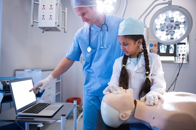 Medico che per mezzo del computer portatile mentre ragazza che esamina un manichino