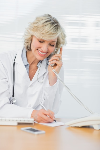 Foto aggiusti facendo uso del telefono mentre scrivono le note all'ufficio medico