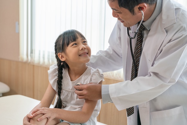 Doctor using stethoscope to examine little girl patient at hospital